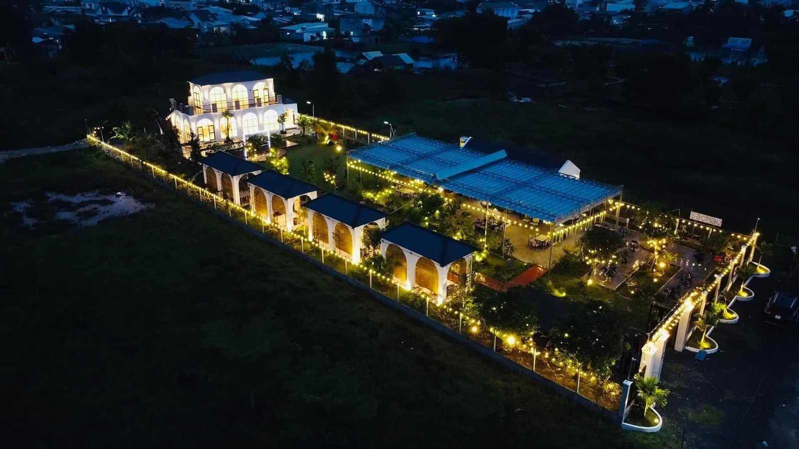 Nhà hàng Sắc Màu Trảng Bàng nhìn từ trên cao đêm — dây đèn vàng giăng giữa cánh đồng